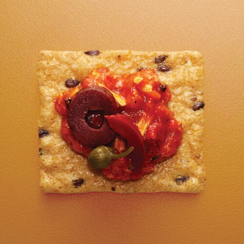 Crunchmaster cracker with red salsa and olives on top.