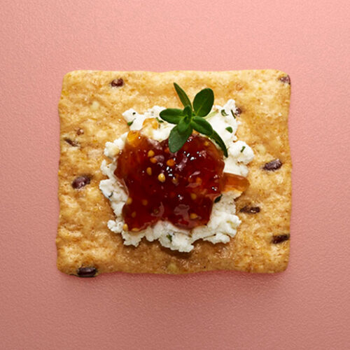 Crunchmaster cracker with cheese and jam on top.