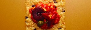 Crunchmaster cracker with red salsa and olives on top.