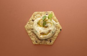 Crunchmaster cracker with hummus and olive oil on top.