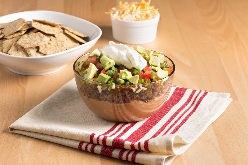 Layered taco dip with Crunchmaster crackers for dipping.